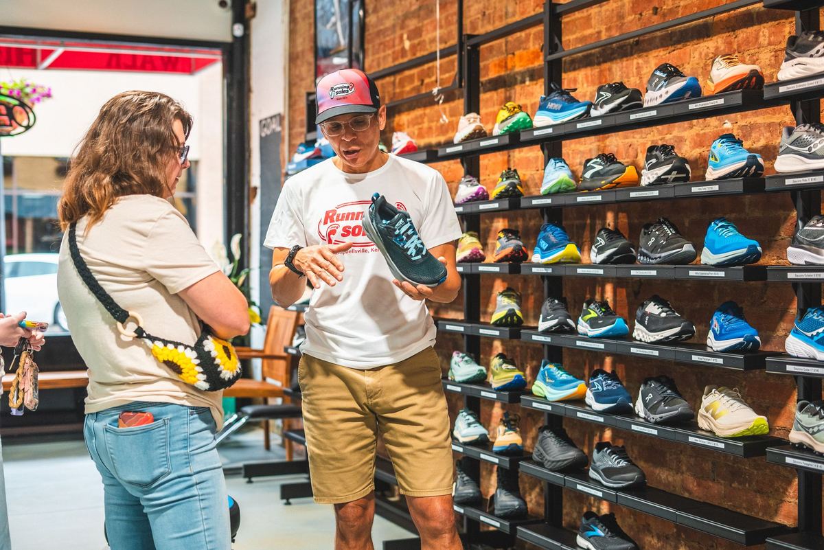 Staff member fitting a customer for running shoes in front of a shoe wall